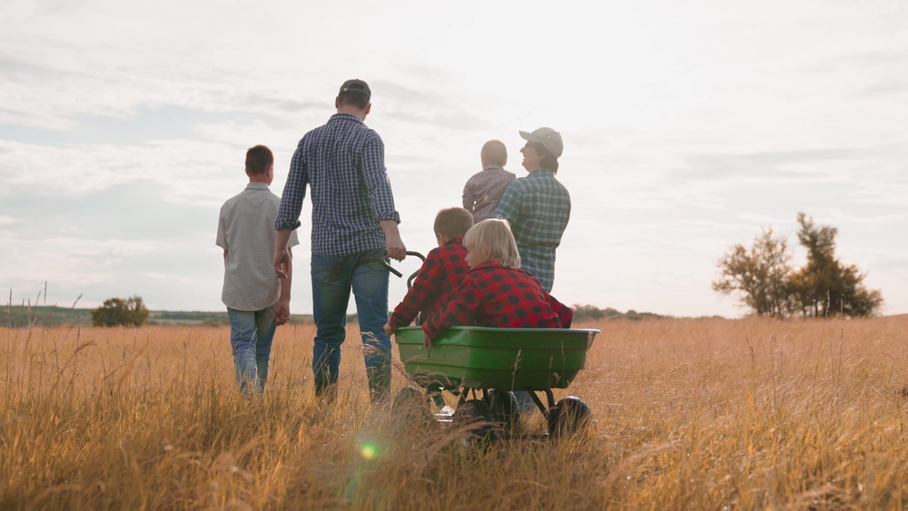 Farmer pulls cart with little children walking with family in country field at sunset light. Happy family with children spending time together on farm field. Farmer family with children in field