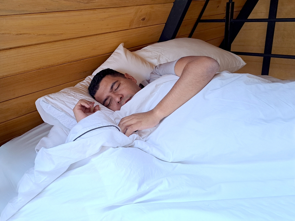A 40-year-old dark-skinned Latino man sleeps between white sheets, suffering from sleep problems such as insomnia, narcolepsy, hypersomnia, snoring and apneas