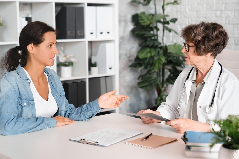 Female middle-aged patient complaining about illness diseases symptoms to elderly senior doctor general practitioner gynecologist in hospital