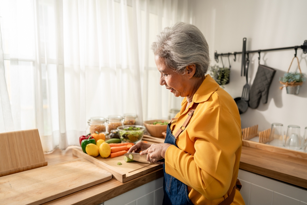 Asian senior elderly woman cooking food for breakfast in kitchen at home. Attractive mature older grandmother wearing apron, spend leisure time making meal for health care during morning time in house
