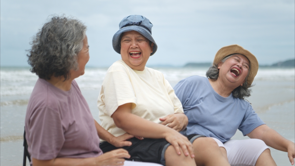 Happy senior women enjoying a playful walk on the beach, laughing and holding hands as they splash through the waves together