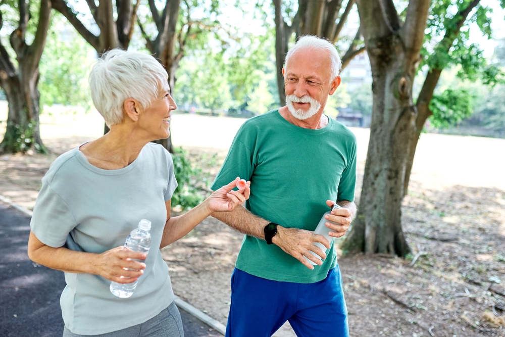 Smiling active senior couple jogging exercising and having fun and laughing together taking and walking  a break in the park