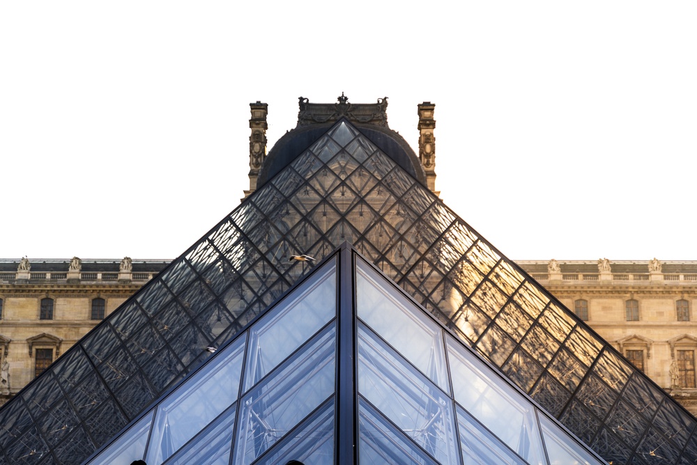 Louvre museum glass pyramid contrasting with historic palace architecture against clear sky