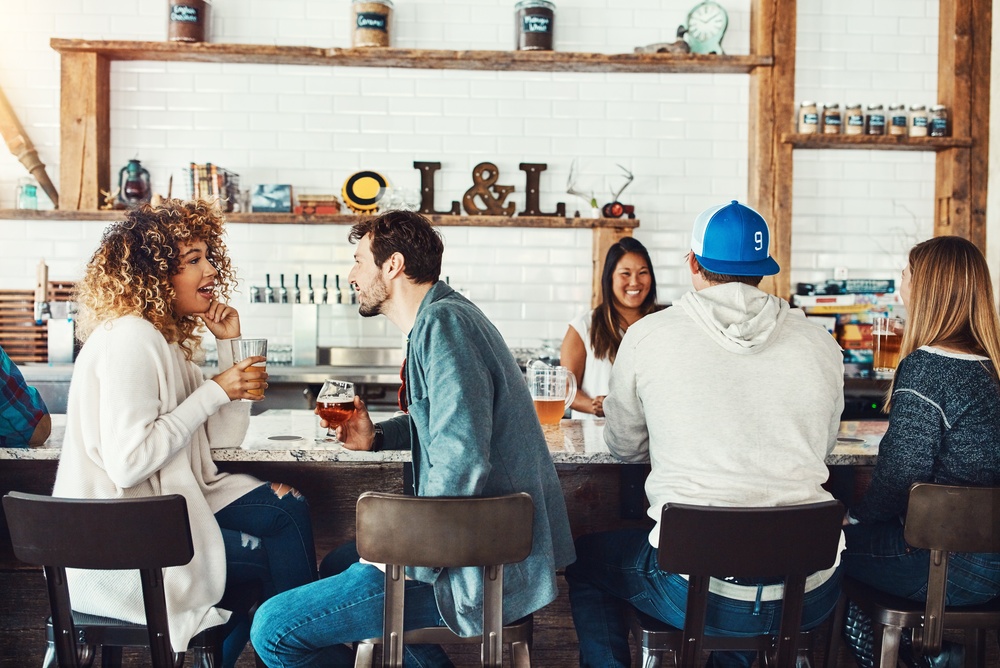 Relax, couple and conversation with drinks at bar for weekend break, story interest or connection. Happy, interracial people and alcohol at pub with talking, bonding together and healthy relationship