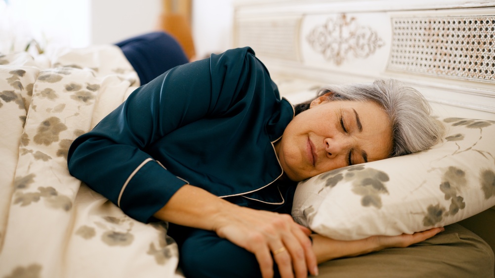 Senior woman resting comfortably in bed, wearing pajamas, enjoying a peaceful night's sleep in a cozy bedroom