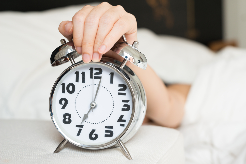 Young woman turns off the alarm clock waking up in the morning.