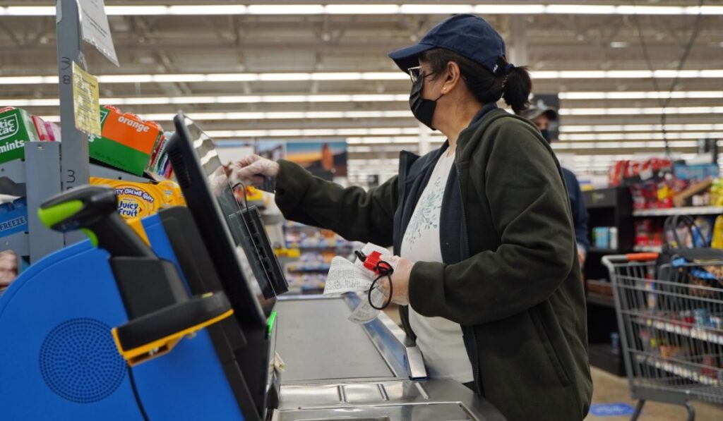 Masked and gloved woman uses the self checkout