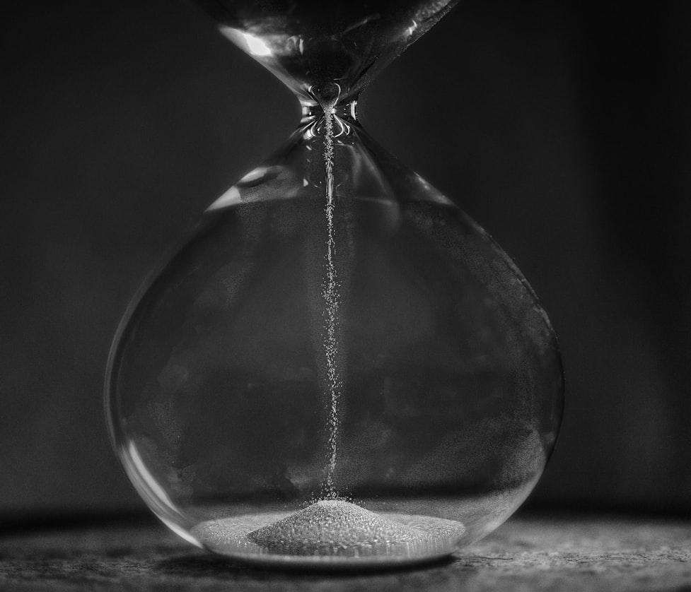 Black and white close-up of an hourglass with sand streaming down into the bottom bulb.