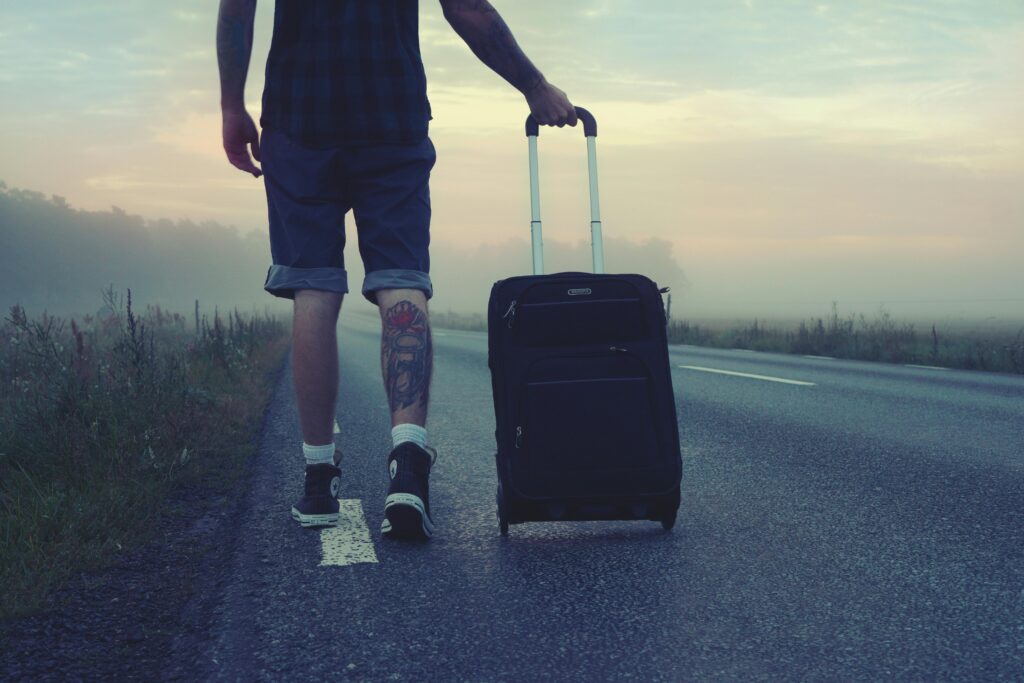 Man walking down a foggy road at dawn, pulling a black suitcase behind him.