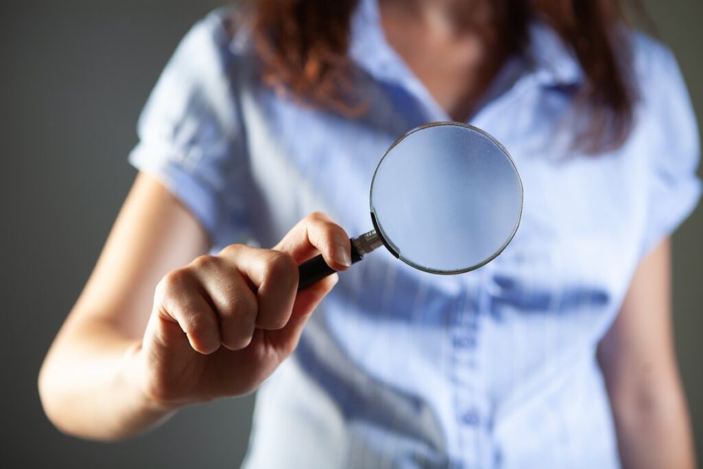 Woman in a blue shirt holding up a magnifying glass toward the viewer.