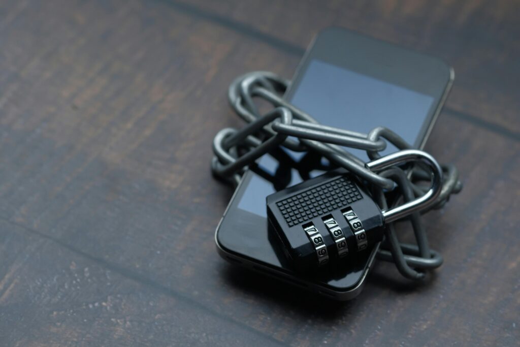 A smartphone wrapped in a heavy metal chain and secured with a combination padlock on a wooden surface.