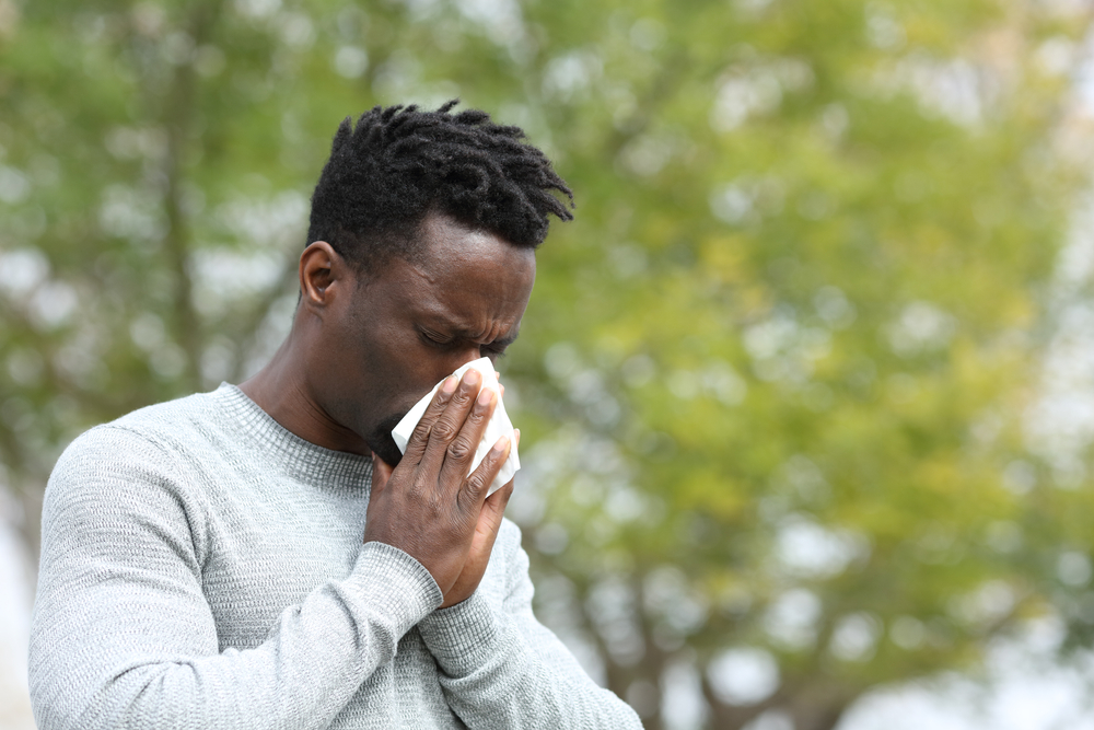 Allergic black man blowing on wipe in a park on spring season a sunny day