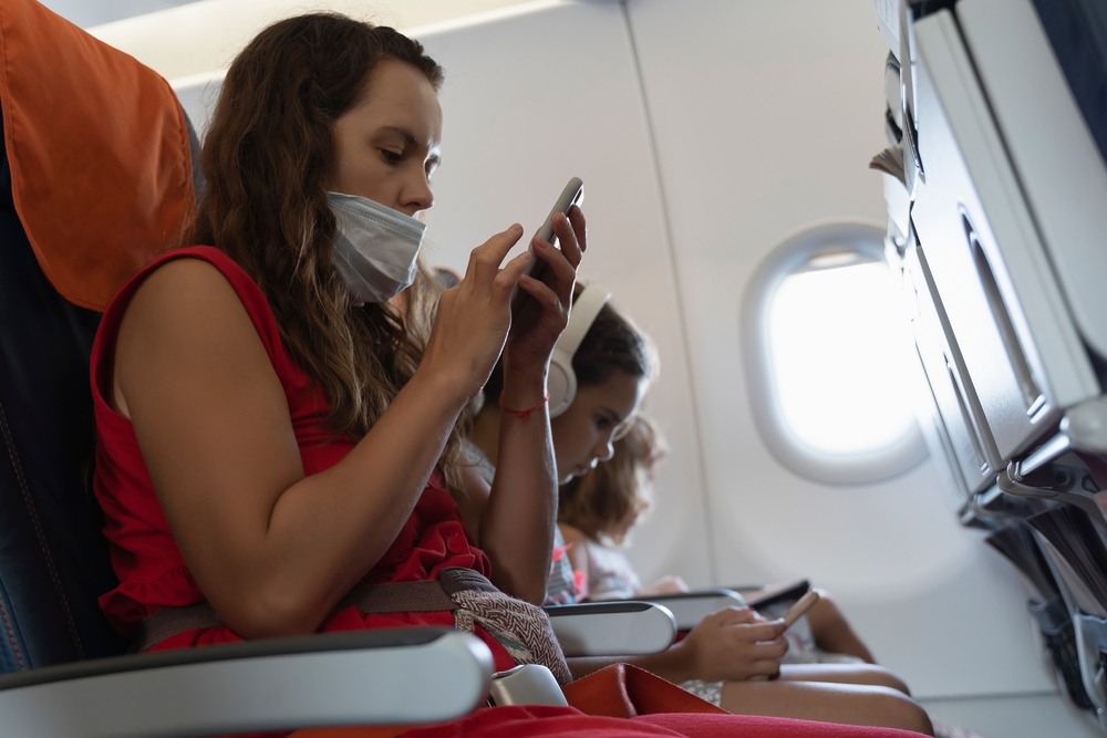 woman wearing a mask and using her smartphone on a flight