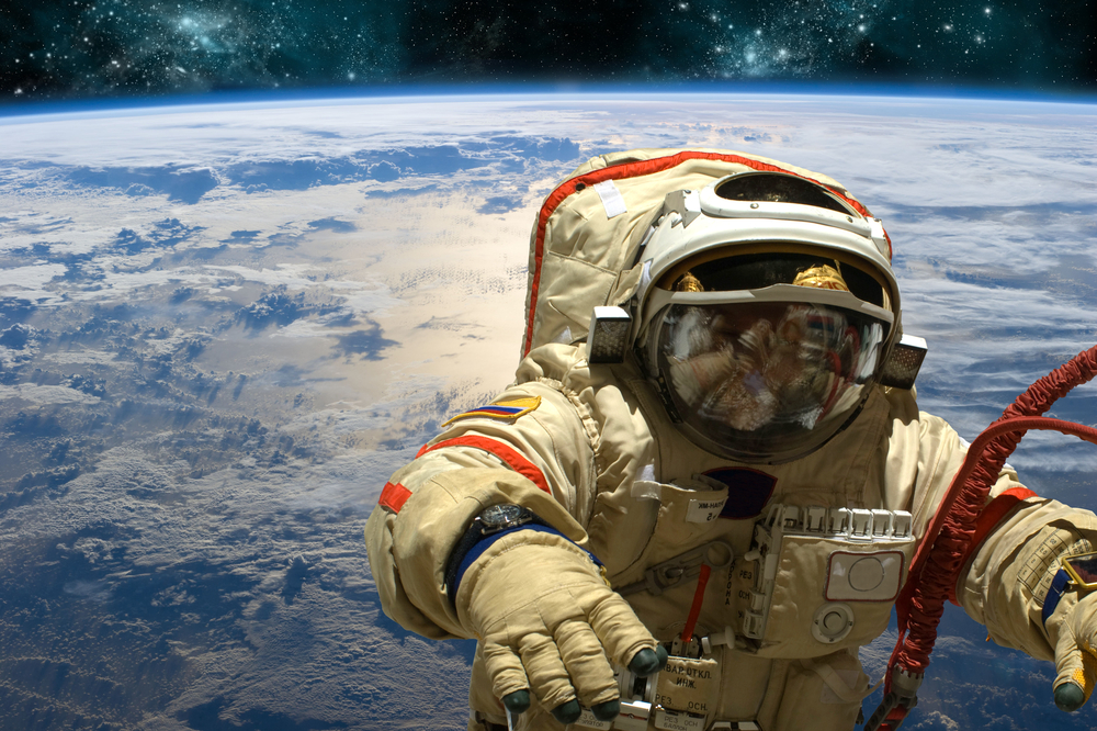 A cosmonaut floats in space above Earth. Stars shine in the background. Elements of this image furnished by NASA.