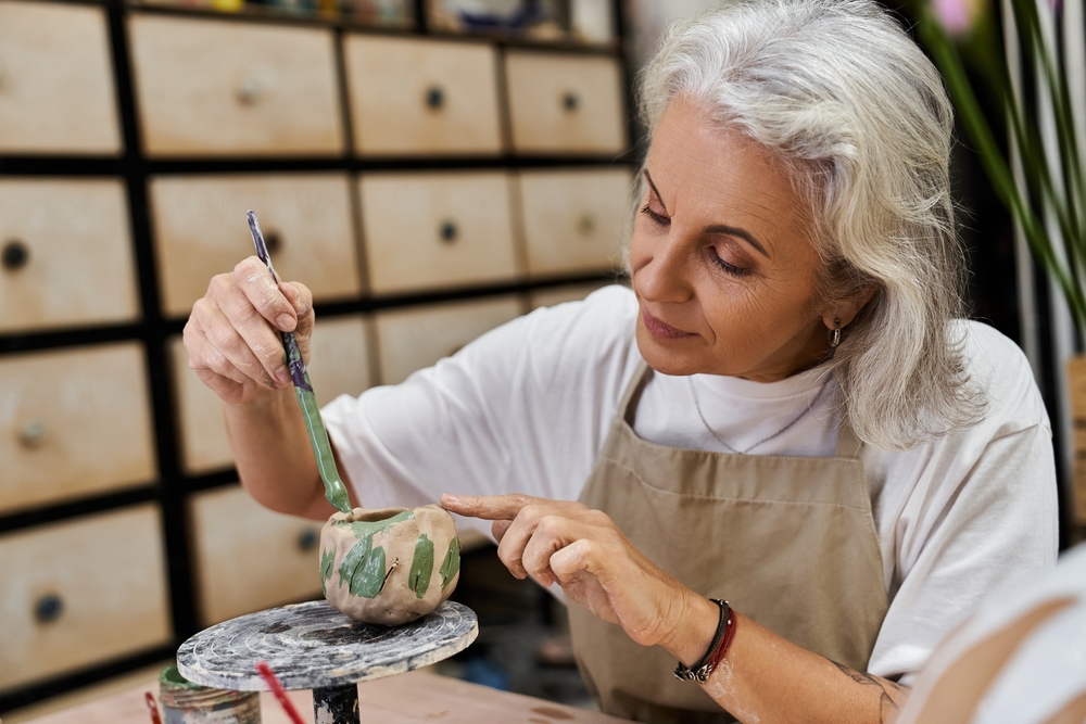 A skilled mature woman focuses on adding details to her pottery project in a vibrant studio.