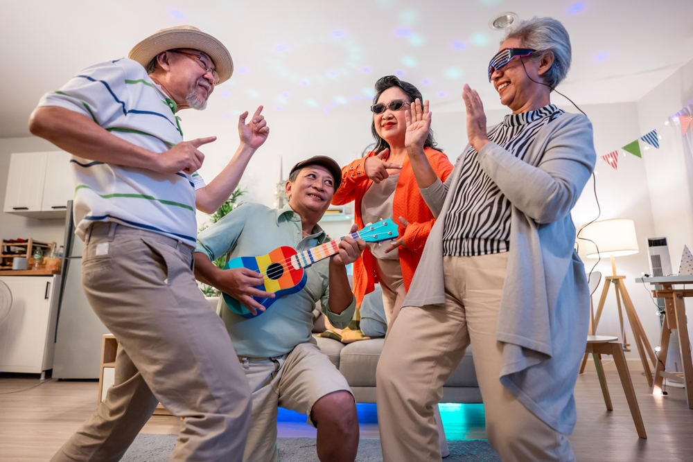 Group of Asian senior friend having evening party in living room at home. Mature elderly man and woman having fun, dancing with cool music while celebrate weekend reunion gathered together in house.