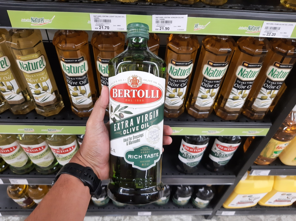 Bangi, Selangor, Malaysia - April 4, 2025: Customer holding a bottle of Bertolli Extra Virgin Olive Oil in a supermarket, surrounded by various brands of olive oil including Naturel on the shelves.
