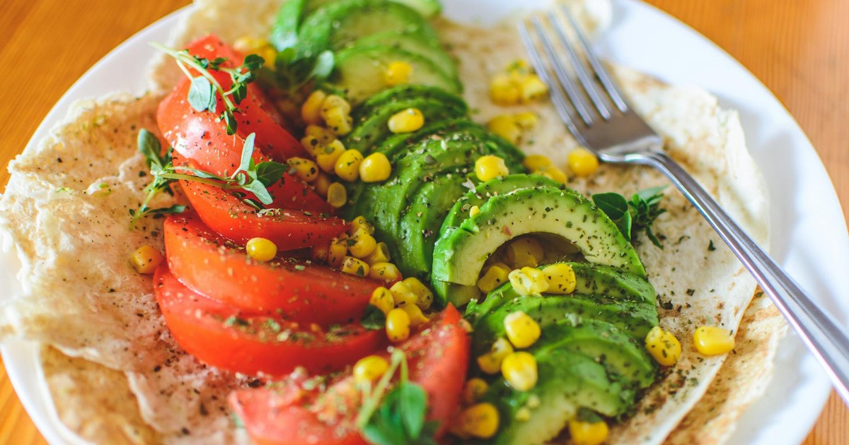 A vibrant salad with avocado, tomato, and corn on flatbread, topped with herbs, perfect for a healthy meal.