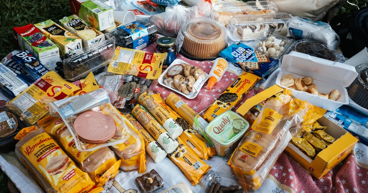 Top view of a picnic setup with diverse snacks, cookies, juices, and packaged foods on a blanket.