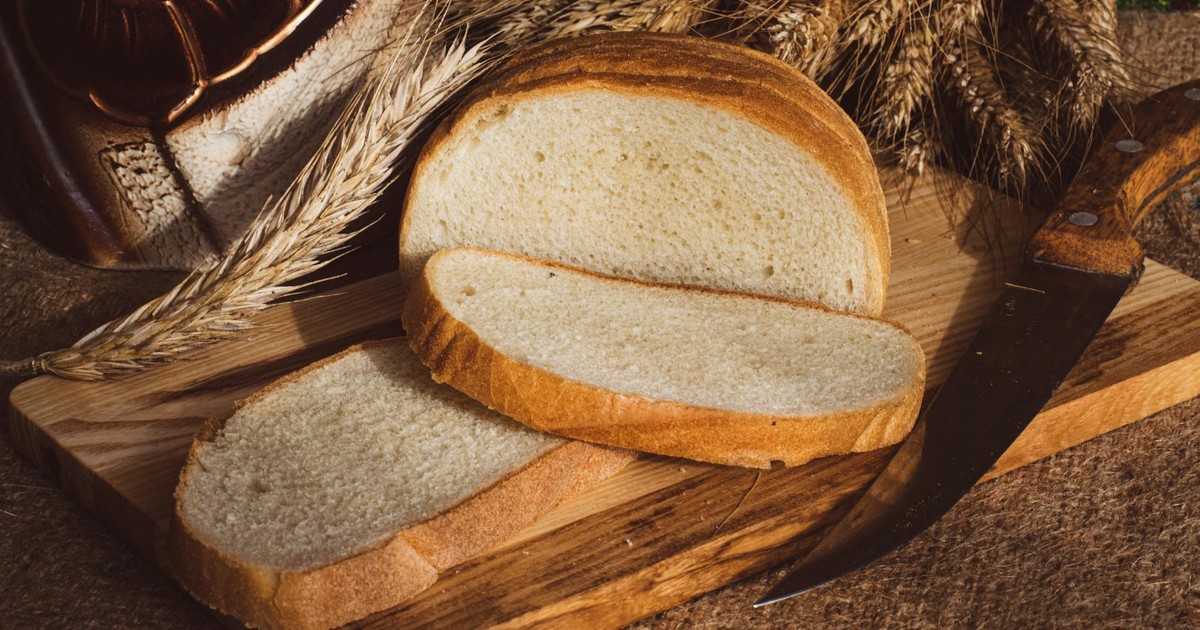Freshly sliced bread on a rustic wooden board with wheat and a knife.