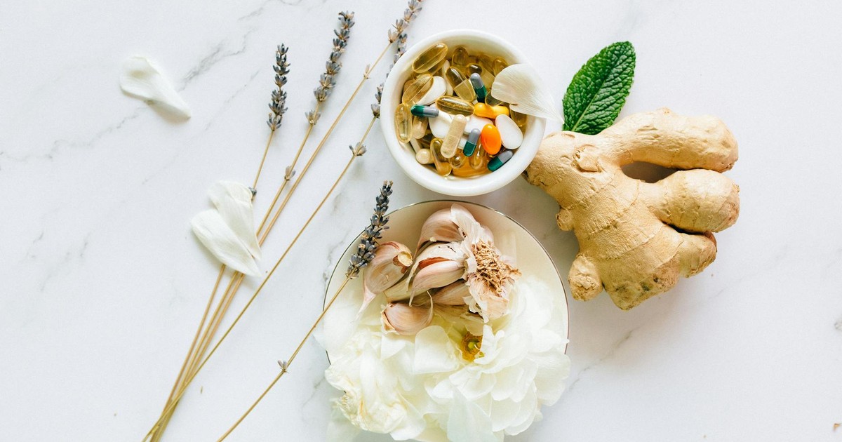Flat lay of ginger, garlic, flowers, and supplements for holistic health.