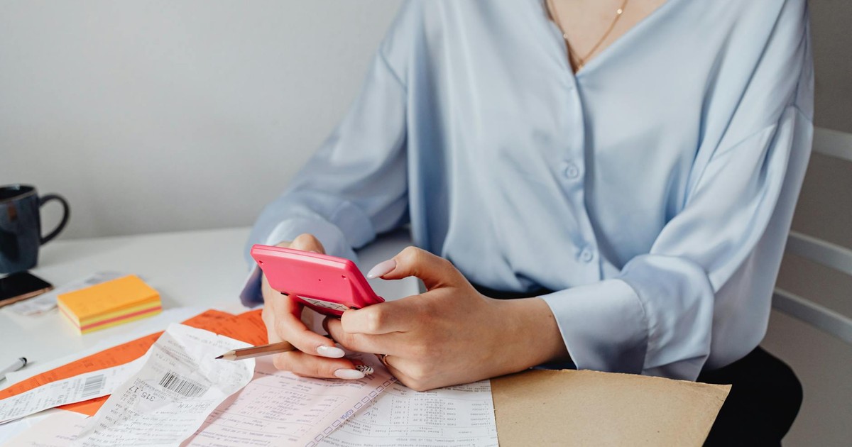 A woman using a pink calculator surrounded by bills and receipts at a desk.