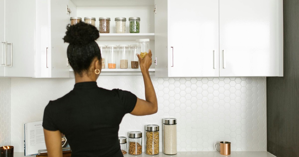 A woman organizing a pantry shelf with various food jars in a modern kitchen.