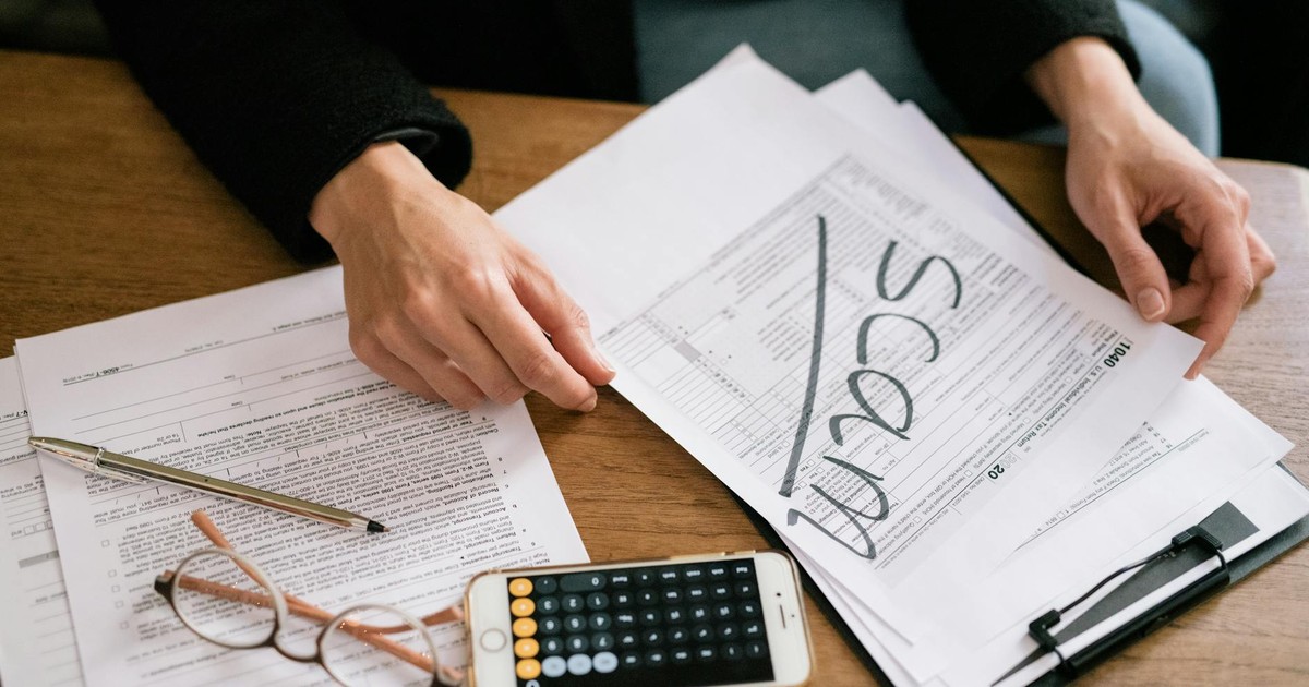 Hands of a person examining tax forms labeled as scam with calculator and papers.