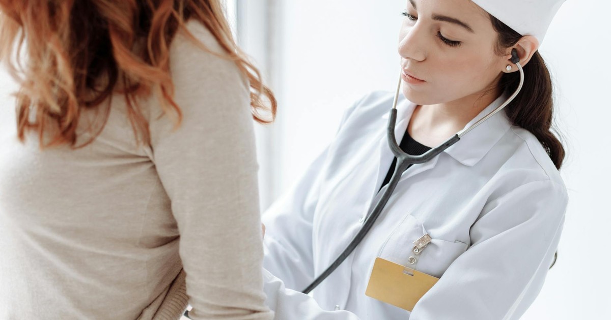 A female doctor in a white coat using a stethoscope during a patient examination.