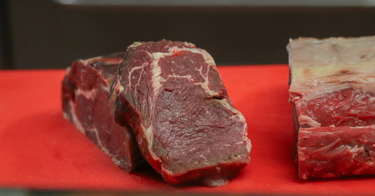 Close-up of raw beef pieces on a red cutting board, showcasing marbling and texture.