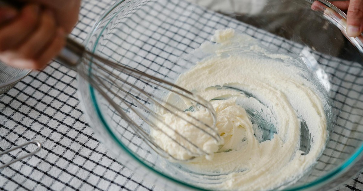 A person whisking cream in a glass bowl on a checkered tablecloth, capturing the art of baking.