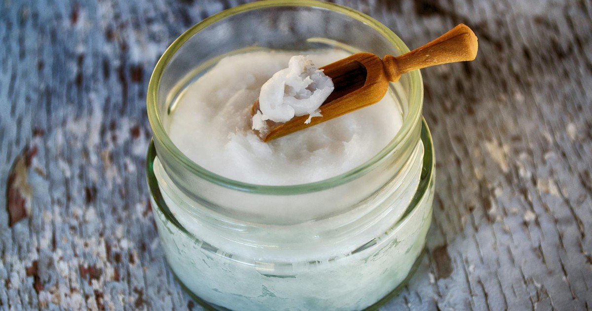 Close-up of organic coconut oil in glass jar with wooden spoon, perfect for natural health and wellness use.