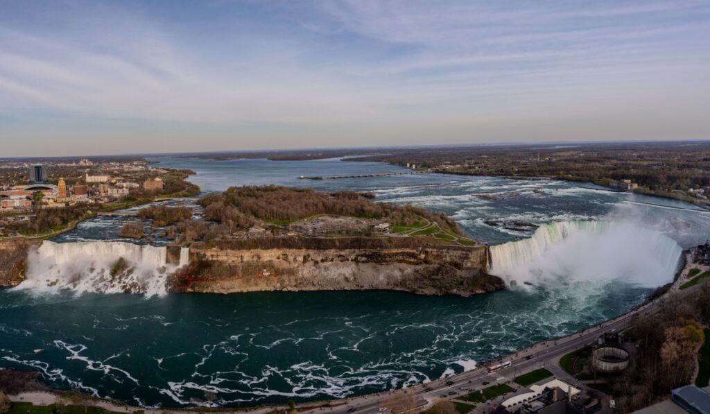 A sweeping aerial panorama captures the American Falls, Bridal Veil Falls, and Horseshoe Falls along the Niagara River between Niagara Falls, New York, and Ontario on a clear day.