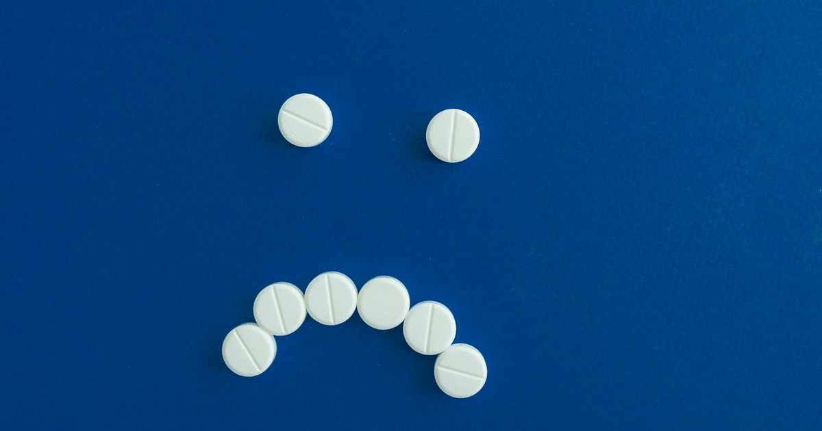White pills arranged in a sad face shape on a solid blue background.