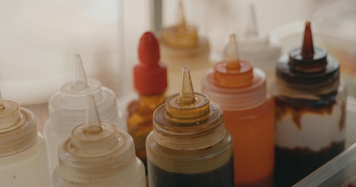 Close-up of various condiment squeeze bottles in a food preparation setting.