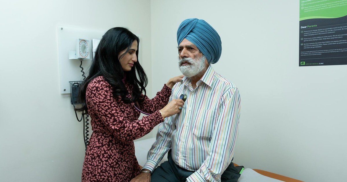 A doctor uses a stethoscope to examine a senior man in an examination room.