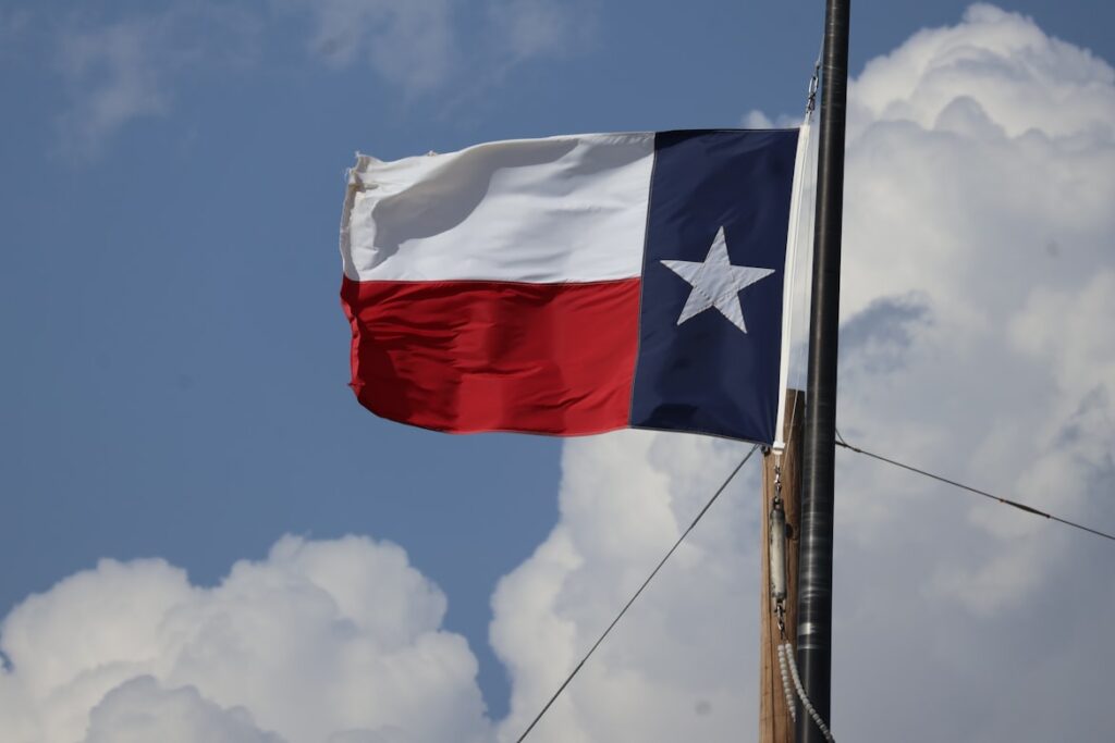 The Texas state flag flying against a blue sky with white clouds.