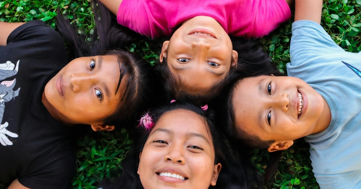 Joyful group of diverse children lying on green grass enjoying a sunny day.