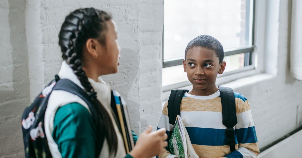 Content multiracial pupils with copybooks and backpacks standing in school corridor and having conversation