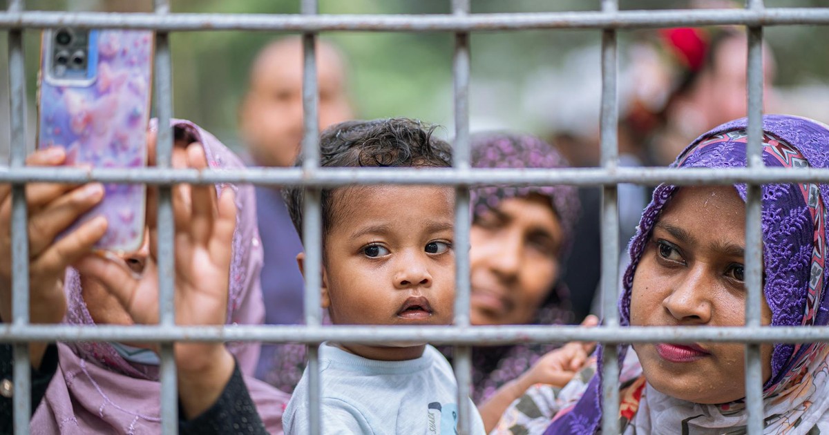A child with adults looking through a metal fence, capturing the moment with a smartphone.