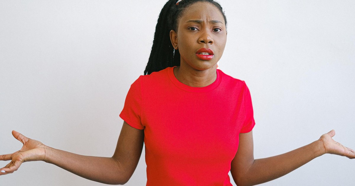 Young black woman in a red shirt with a confused expression. Perfect for emotive stock photo needs.