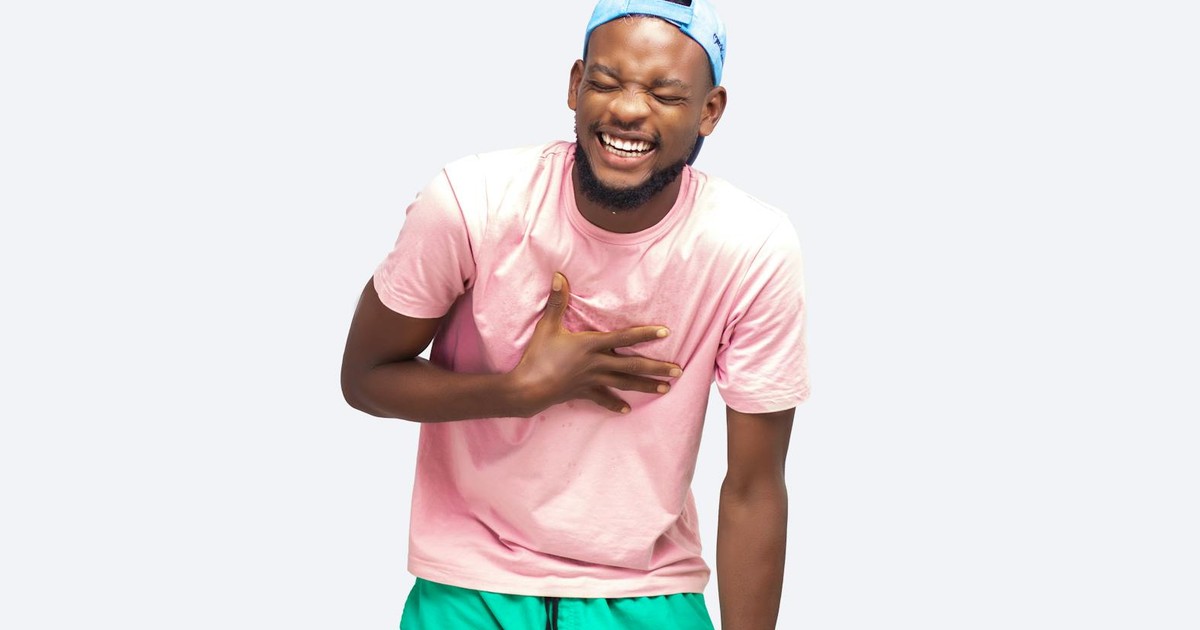 A young man in a pink shirt and green shorts laughing joyfully in a studio setting.