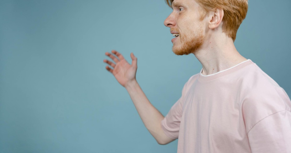 Side profile of a bearded man gesturing against a blue background, expressing emotions.