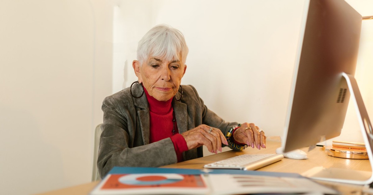 Senior woman in business attire focusing on her work at a modern office desk.