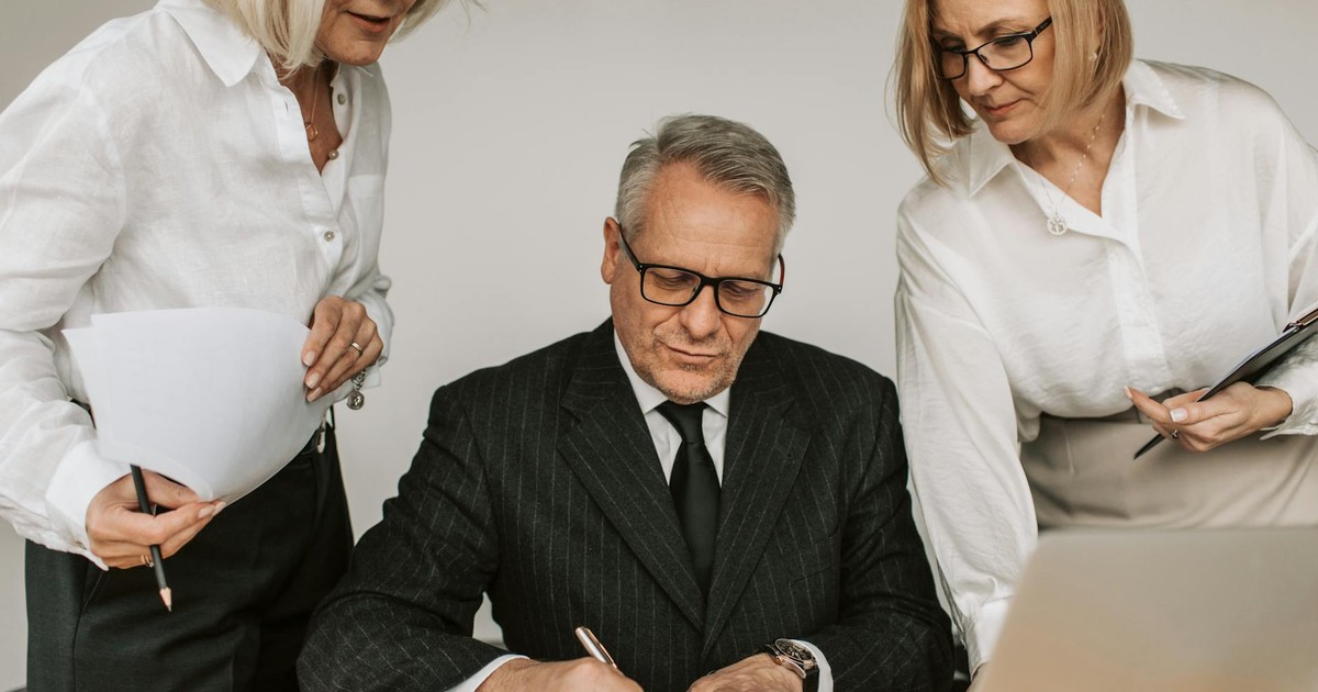 Senior professionals in an office setting reviewing and signing business documents together.