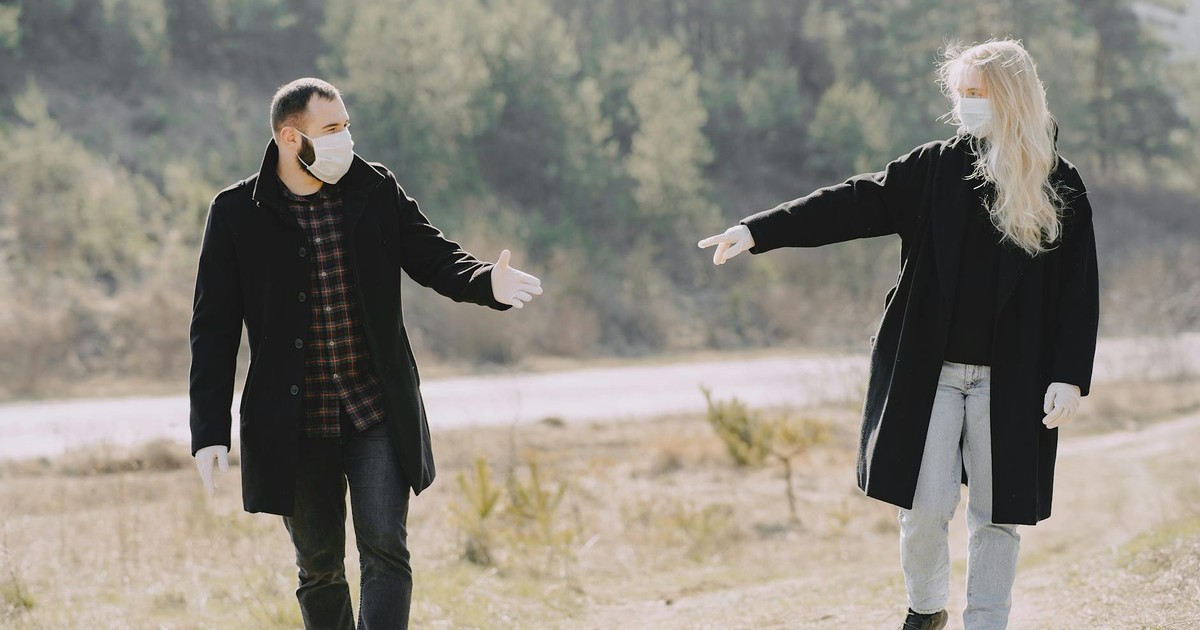 Casual couple in warm coats and protective masks latex gloves looking pulling hands to each other during weekend stroll together