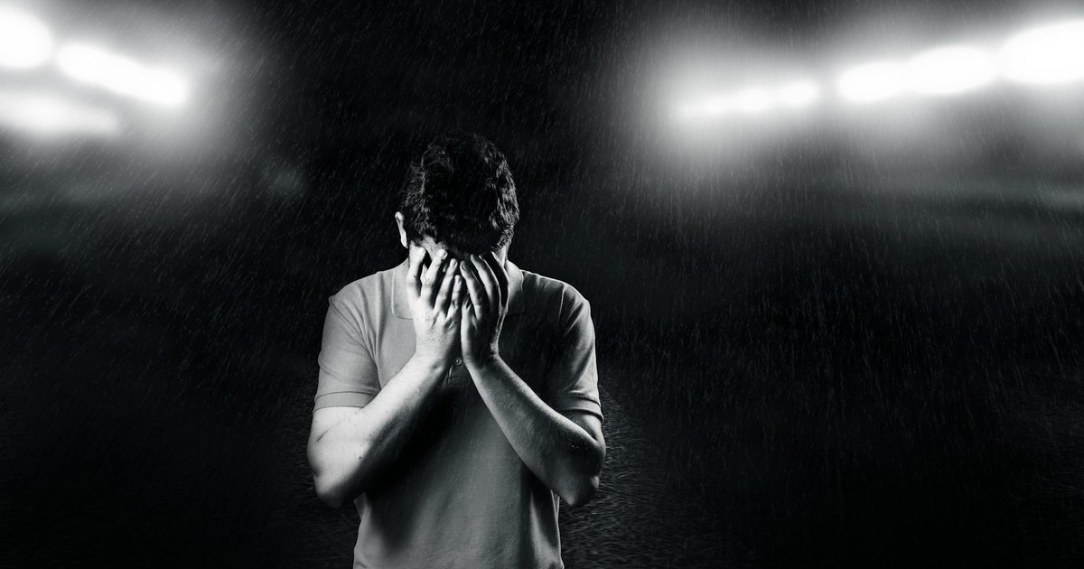 Black and white photo of a man covering his face, conveying emotion and solitude.