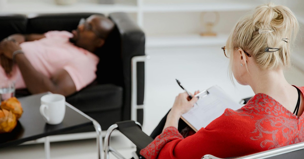 A professional therapist takes notes during a therapy session, engaging with a client.