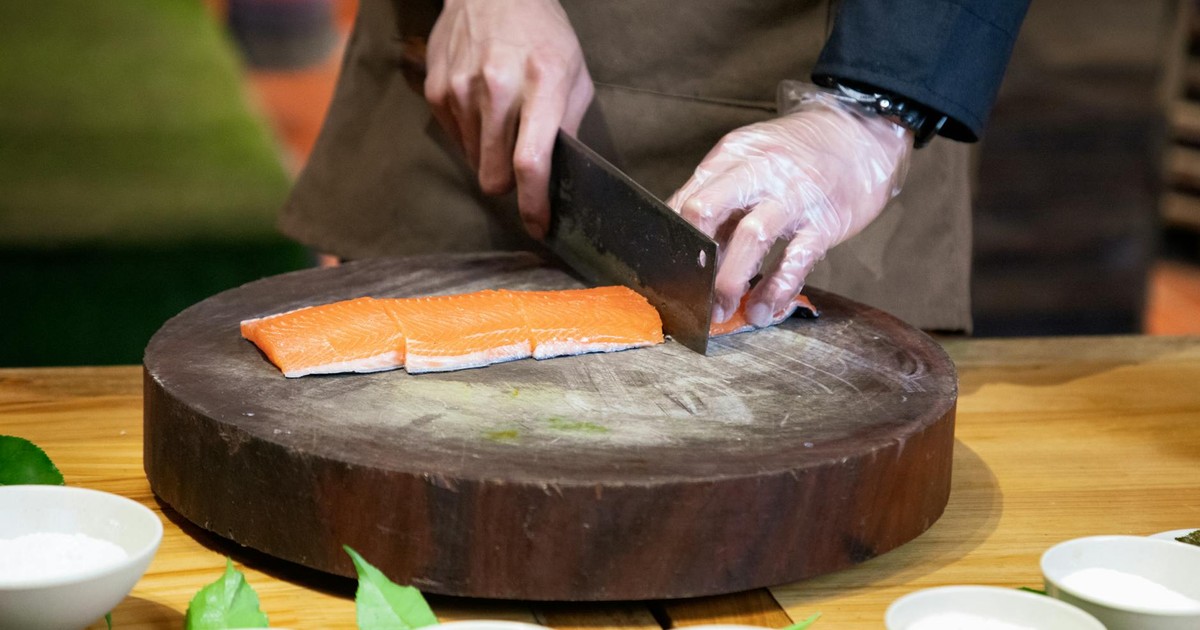 A chef skillfully cuts fresh salmon on a wooden board, surrounded by kitchen ingredients.