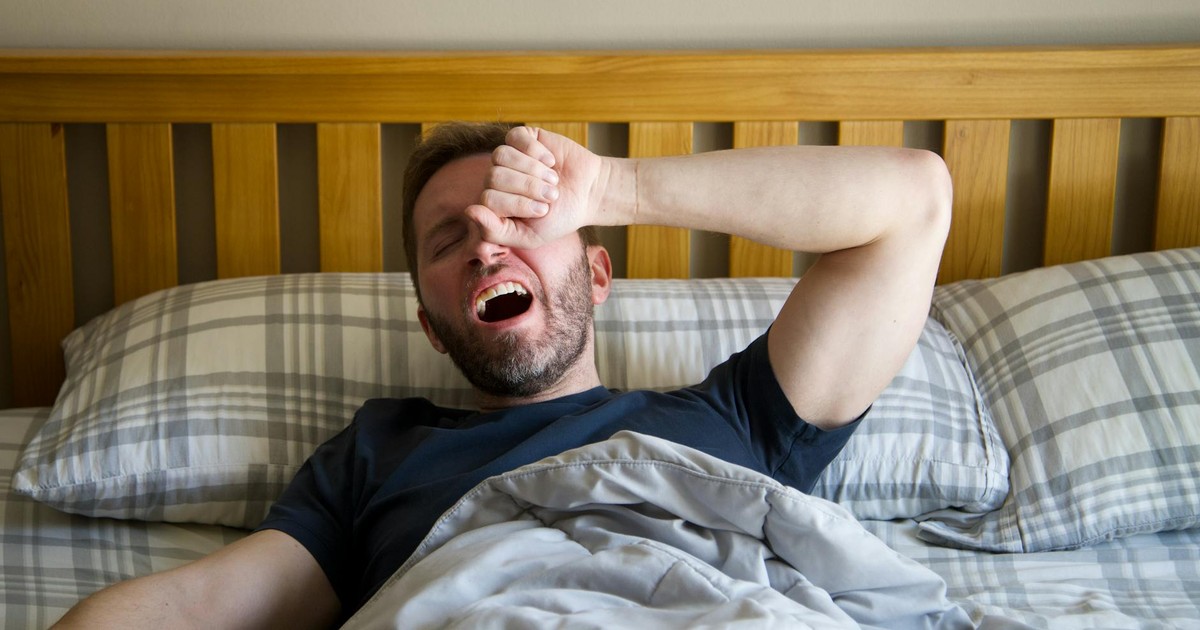 Man yawning and waking up in bed, starting a new day with the morning light.